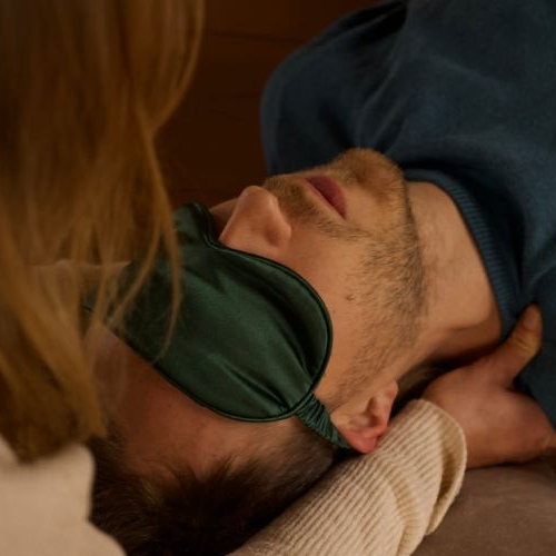 A breathwork facilitator holds man's shoulder's whilst he has a mask on his eyes and is breathing during conscious connected breathwork session.